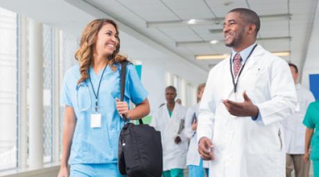 Two people talking while walking in hospital Doctor in white coat and person in scrubs talking while walking down hospital hallway